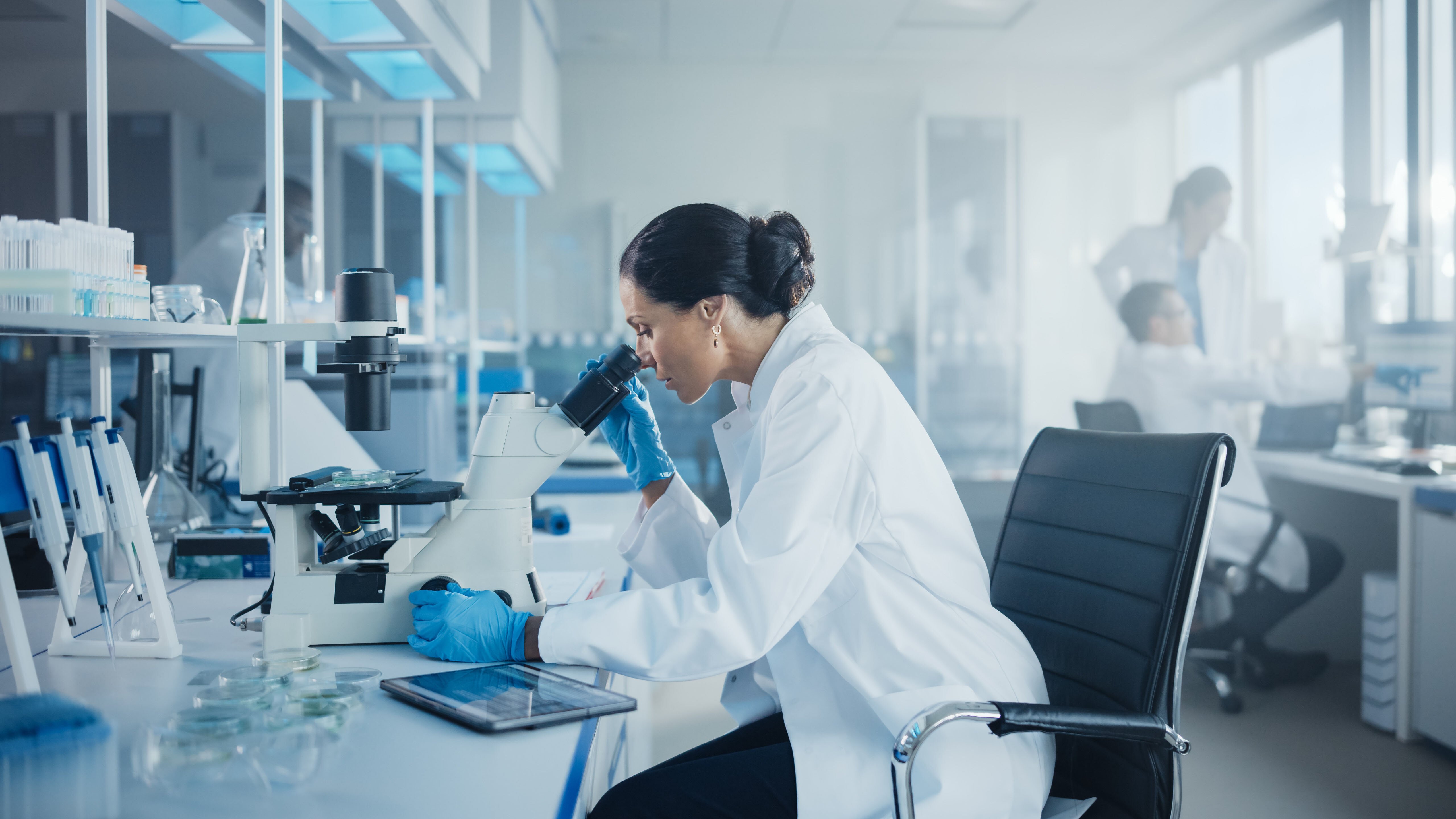Female working in lab looking at microscope_AdobeStock_402341501