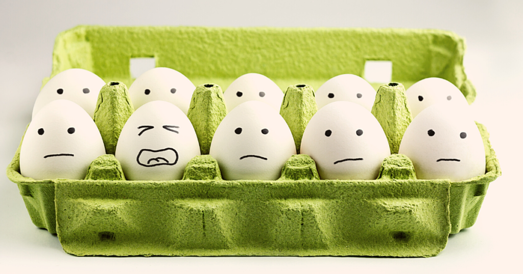 10 white eggs in green carton with sad faces except one that looks stressed