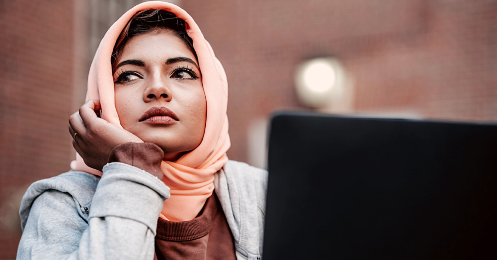 woman with pink head scarf and laptop contemplating her job search