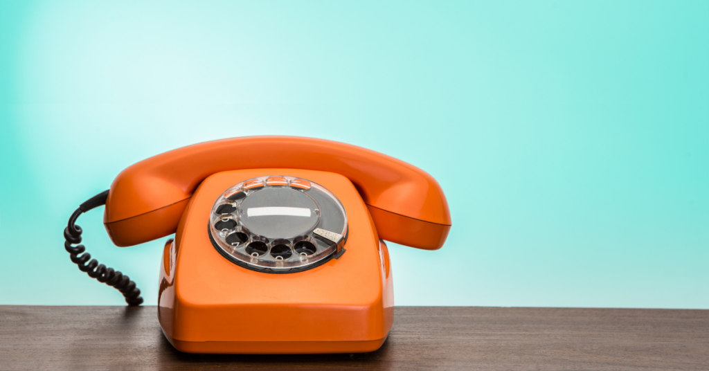 orange rotary phone in front of teal wall