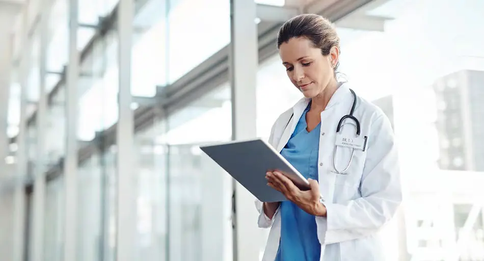 Woman in healthcare profession standing while working on tablet device.